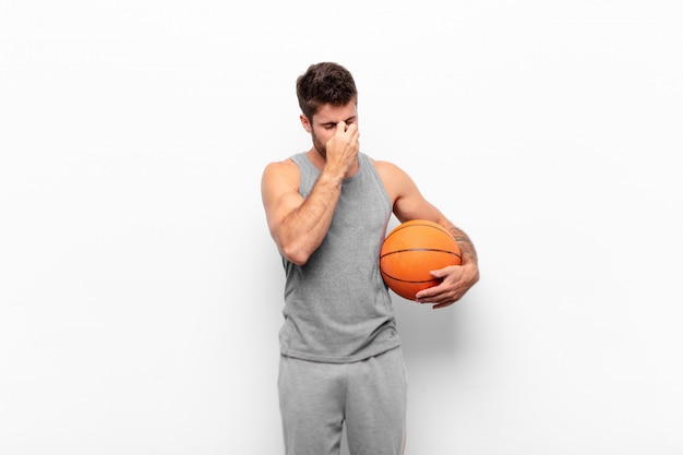 若いハンサムな男は、ストレスを感じ、不満と欲求不満を感じ、額に触れ、バスケットボールのボールを保持している激しい頭痛の片頭痛に苦しんでいます。