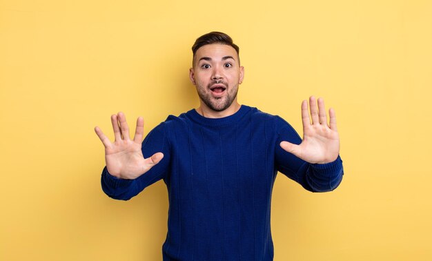 Young handsome man feeling stupefied and scared, fearing something frightening, with hands open up front saying stay away