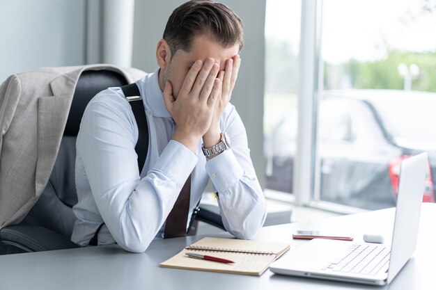 Young handsome man feeling tired and frustrated sitting at his working place