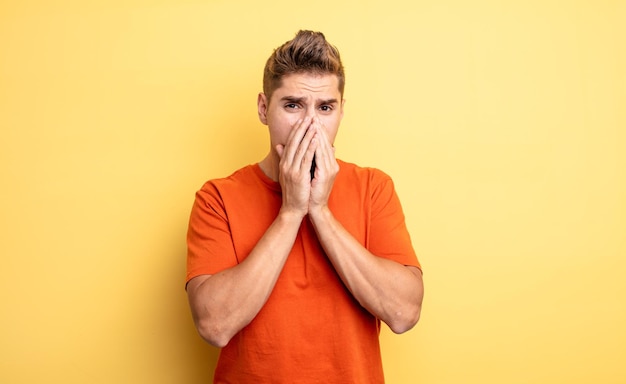 young handsome man feeling worried, upset and scared, covering mouth with hands, looking anxious and having messed up. strange moustache concept