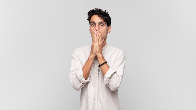 young handsome man feeling worried, upset and scared, covering mouth with hands, looking anxious and having messed up