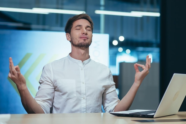 Foto giovane uomo d'affari libero professionista manager in ufficio al tavolo in appoggio chiuso gli occhi medita mostra le sue mani pose yoga