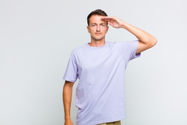 Young handsome man greeting the camera with a military salute in an act of honor and patriotism, showing respect