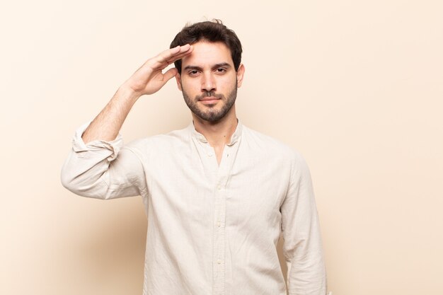 young handsome man greeting the camera with a military salute in an act of honor and patriotism, showing respect