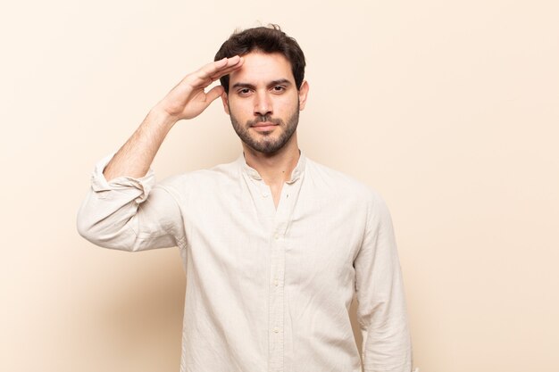 Young handsome man greeting the camera with a military salute in an act of honor and patriotism, showing respect