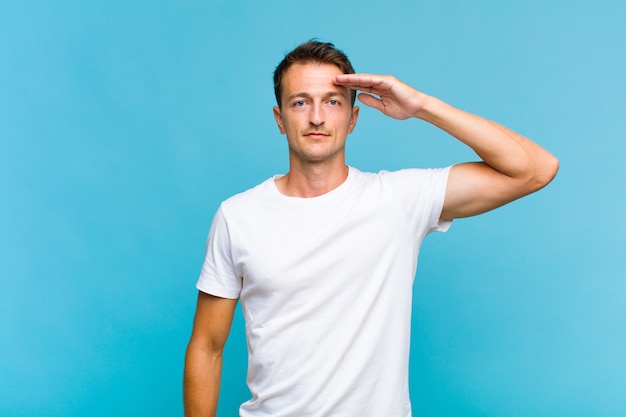 Young handsome man greeting with a military salute in an act of honor and patriotism, showing respect