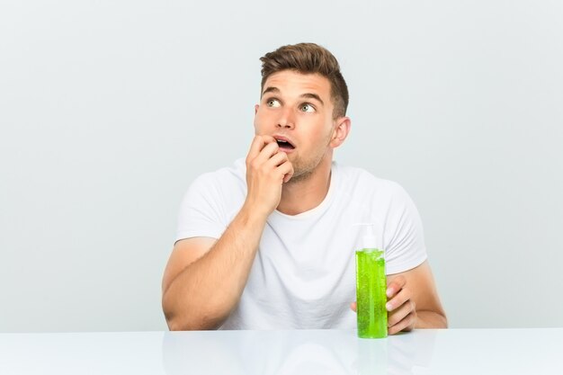 Young handsome man holding a aloe vera bottle relaxed thinking about something looking at a copy space.