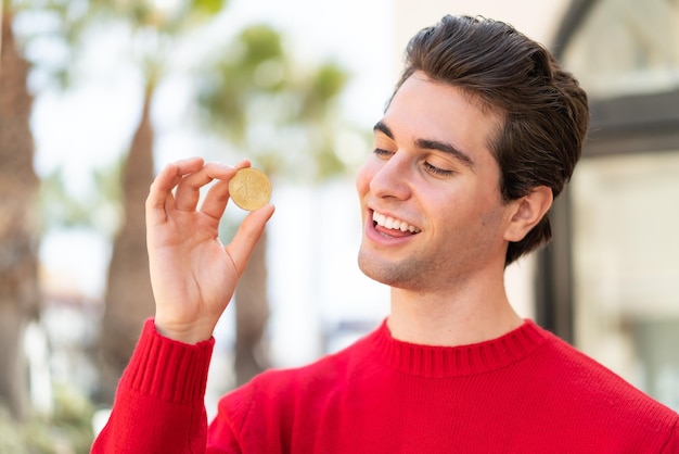 Young handsome man holding a Bitcoin and looking it