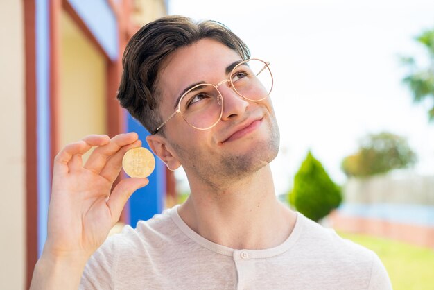 Young handsome man holding a bitcoin and looking up