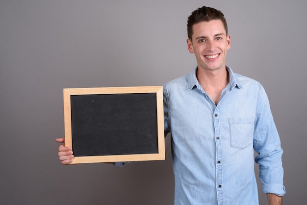 young handsome man holding blackboard on gray