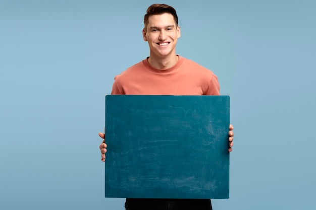 Young handsome man holding blank empty banner looking positive