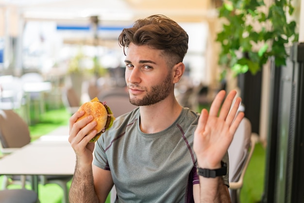 Молодой красивый мужчина держит гамбургер и делает знак "стоп"