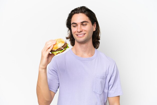 행복 한 표정으로 흰색 배경에 고립 된 햄버거를 들고 젊은 잘 생긴 남자