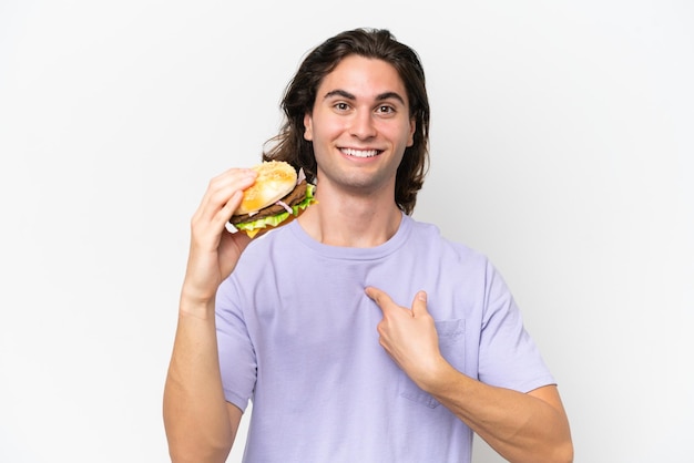 Молодой красивый мужчина держит бургер на белом фоне с удивленным выражением лица