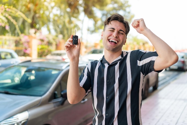 車のキーを保持し、勝利を祝っている若いハンサムな男