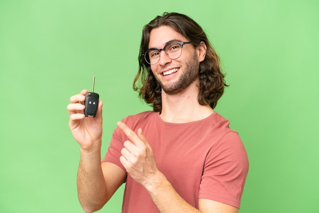 Young handsome man holding car keys over isolated background and pointing it