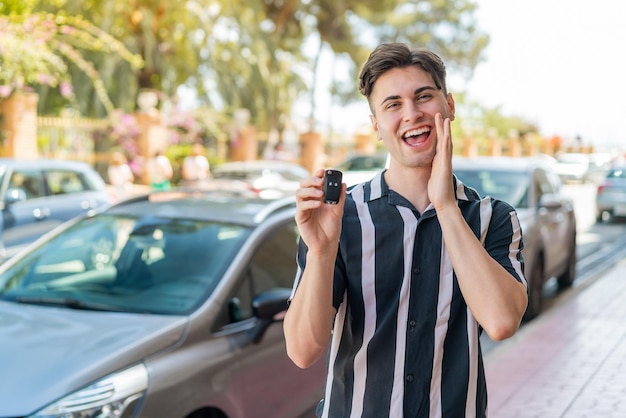 Young handsome man holding car keys at outdoors shouting with mouth wide open