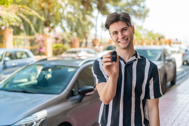 Young handsome man holding car keys at outdoors with happy expression