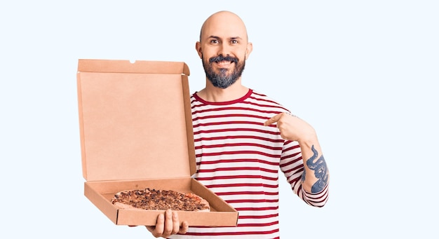 Young handsome man holding delivery pizza box pointing finger to one self smiling happy and proud