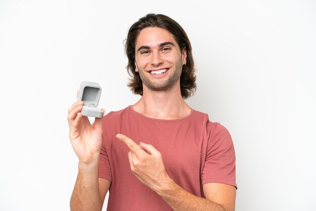 Young handsome man holding a engagement ring isolated on white background and pointing it