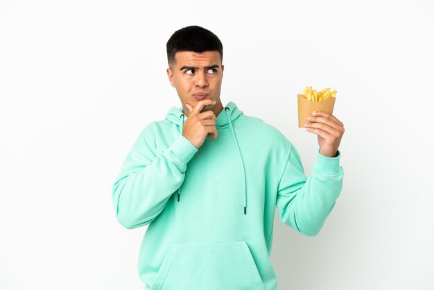 Photo young handsome man holding fried chips over isolated white background having doubts and thinking