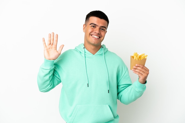 Young handsome man holding fried chips over isolated white background saluting with hand with happy expression