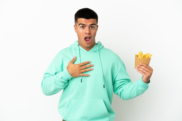 Young handsome man holding fried chips over isolated white background surprised and shocked while looking right