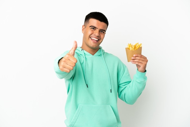Young handsome man holding fried chips over isolated white background with thumbs up because something good has happened