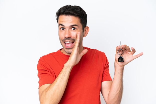 Young handsome man holding home keys isolated over isolated white background whispering something