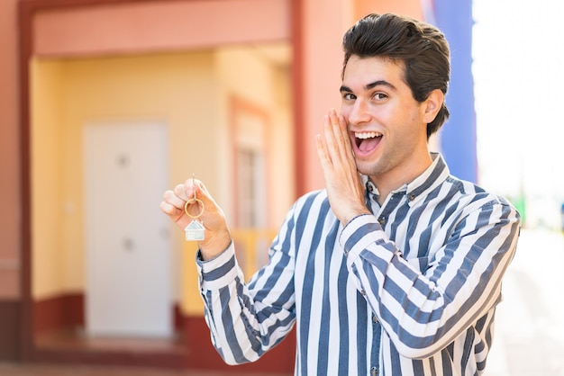 Young handsome man holding home keys at outdoors whispering something