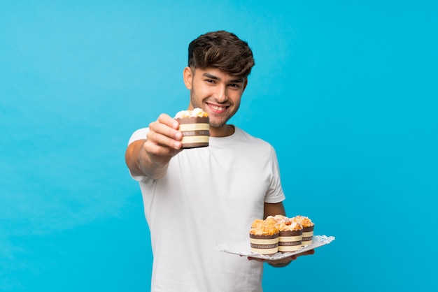 Young handsome man holding mini cakes and offering it