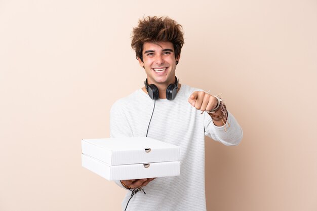 孤立した壁にピザをかざす若いハンサムな男が自信を持って表現であなたに指を指す