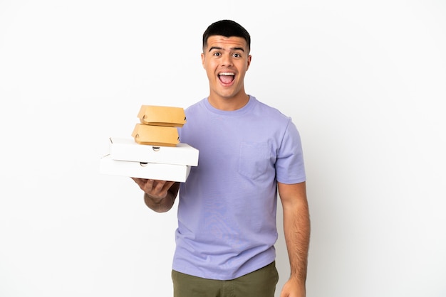 Young handsome man holding pizzas and burgers over isolated white background with surprise facial expression