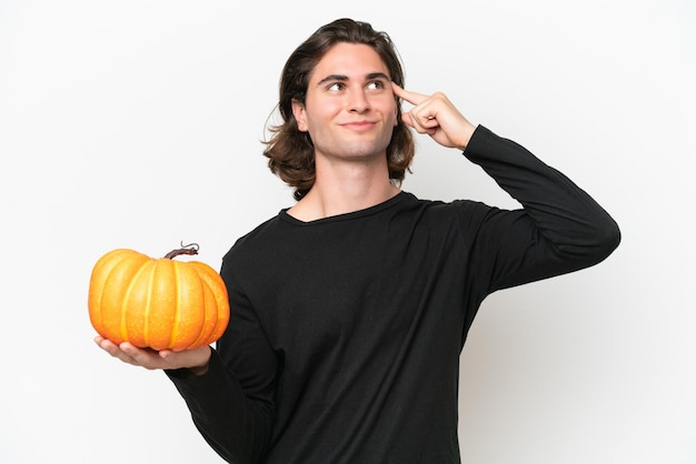 Giovane uomo bello che tiene una zucca isolata su sfondo bianco con dubbi e pensare