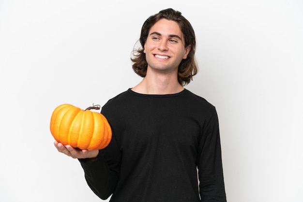 Foto giovane uomo bello che tiene una zucca isolata su sfondo bianco che guarda al lato e sorridente