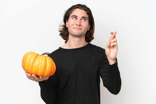 Foto giovane uomo bello che tiene una zucca isolata su sfondo bianco con le dita incrociate e augurando il meglio