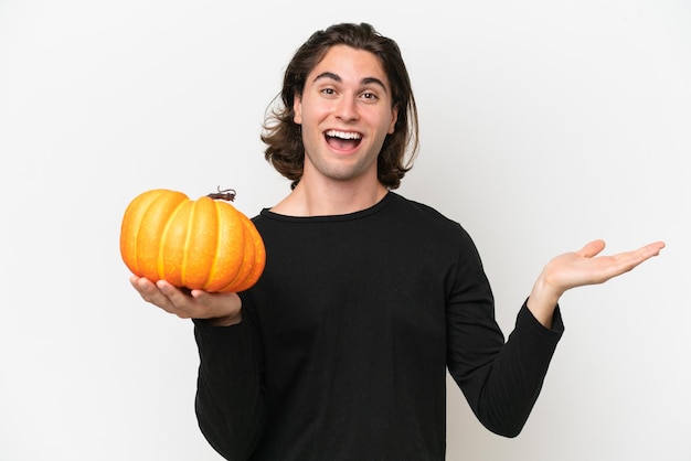 Young handsome man holding a pumpkin isolated on white background with shocked facial expression