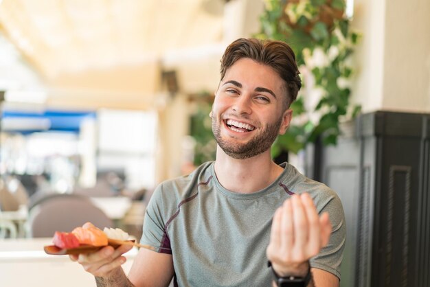 屋外で刺身を持つ若いハンサムな男が手で来るように誘っていますあなたが来てくれて嬉しいです