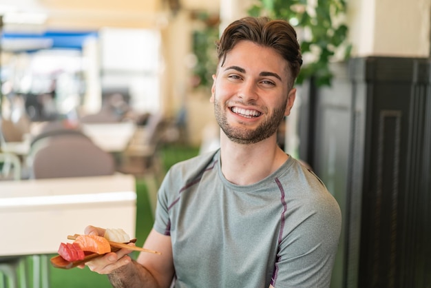 Young handsome man holding sashimi at outdoors smiling a lot