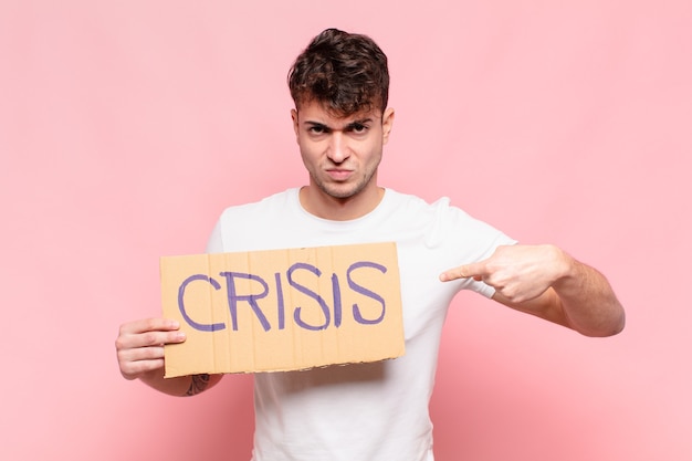 Young handsome man holding a sign with the text CRISIS