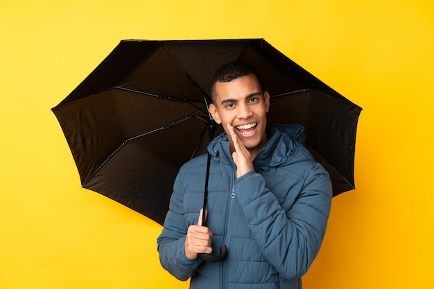 Молодой красивый мужчина держит зонтик над желтой стене шепчет что-то