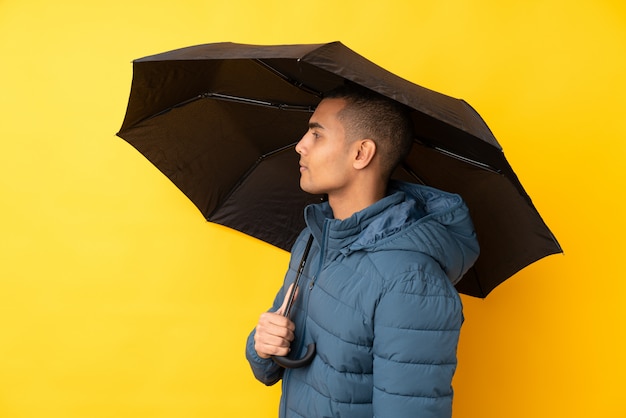 Young handsome man holding an umbrella over isolated yellow wall with happy expression