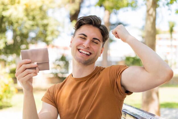 Photo young handsome man holding a wallet and celebrating a victory