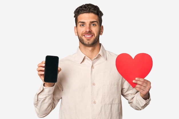 A young handsome man holds a heart shape and a mobile phone concept of internet dates