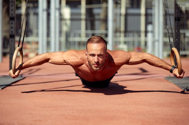 Young and handsome man is doing some pushups He is using loops for that