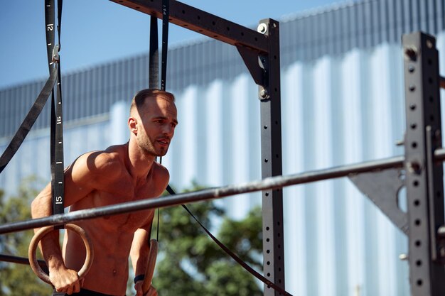 Photo young and handsome man is doing some pushups he is using loops for that