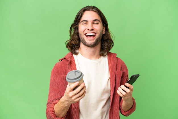 Giovane uomo bello sopra fondo isolato tenendo il caffè da portare via e un cellulare