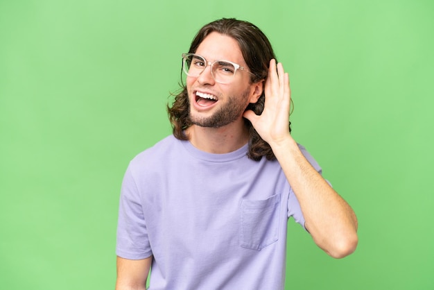 Young handsome man over isolated background listening to something by putting hand on the ear