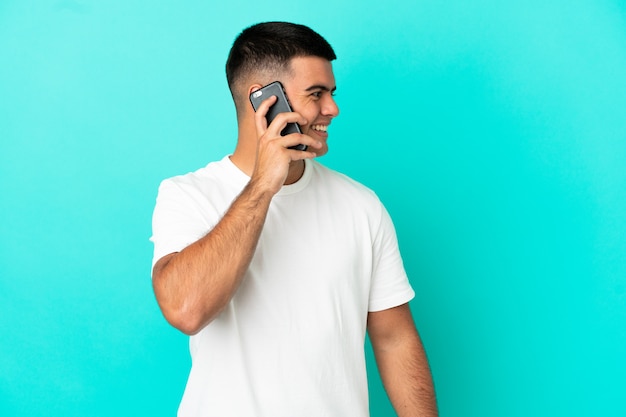 Young handsome man over isolated blue background keeping a conversation with the mobile phone with someone