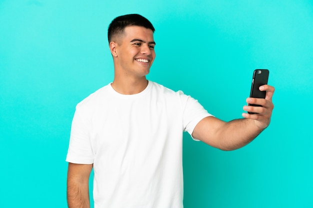 Young handsome man over isolated blue background making a selfie with mobile phone